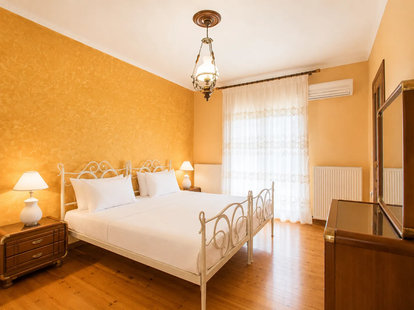 Master bedroom with golden walls, iron bed and lace curtains at Villa Viktoria, Skiathos