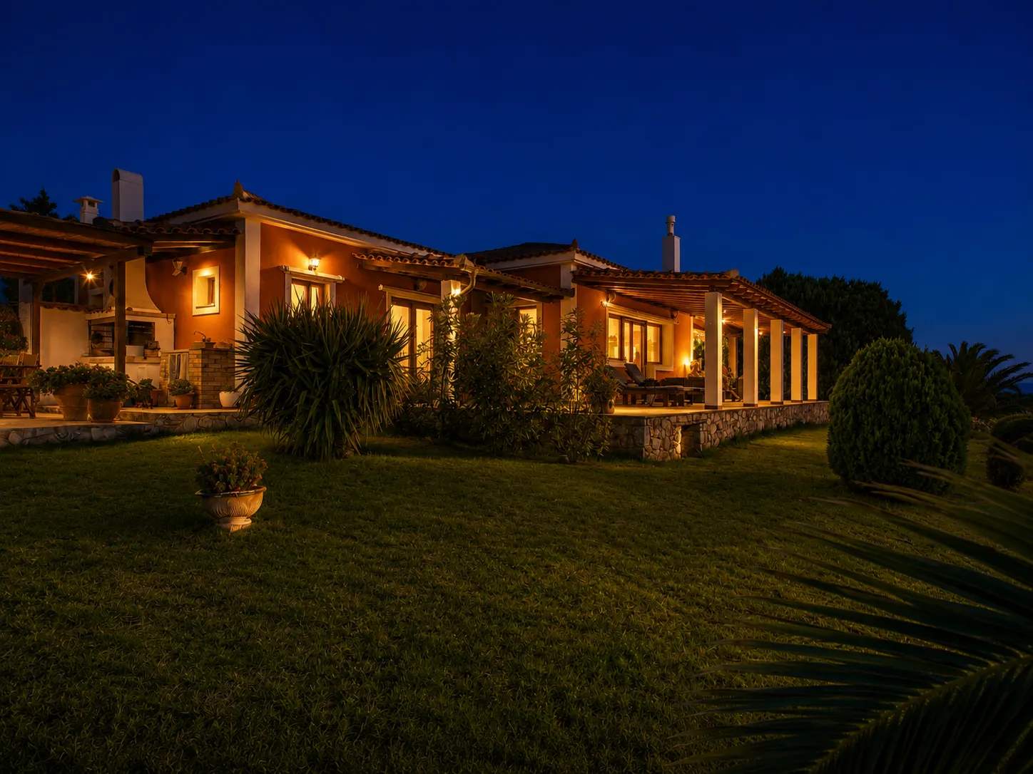 Villa Viktoria exterior illuminated at dusk above a manicured lawn, Skiathos